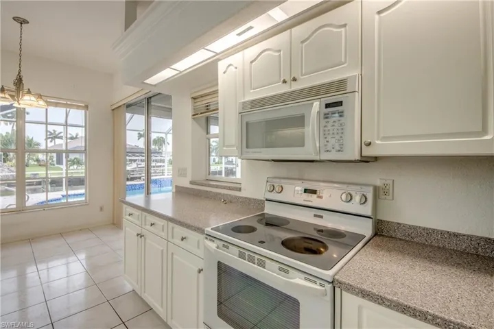 Kitchen featuring an inviting chandelier, hanging light fixtures, white appliances, and a healthy amount of sunlight