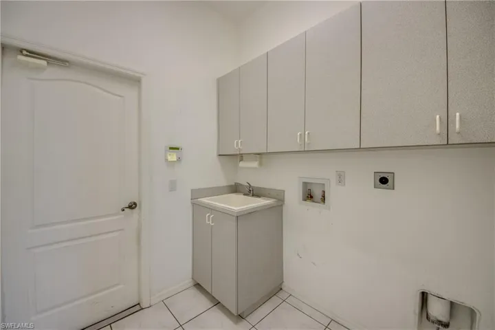 Laundry area featuring hookup for an electric dryer, sink, cabinets, hookup for a washing machine, and light tile patterned floors.  Home does NOT come with Washer/Dryer