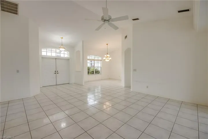 Unfurnished room with ceiling fan with notable chandelier, a towering ceiling, and light tile patterned floors.  Looking back to the front doors and into Dining Room, could easily be made into 4th Bedroom