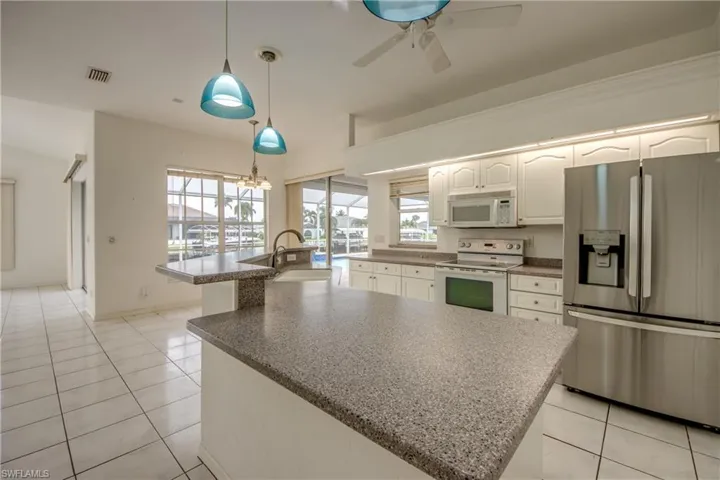 Kitchen with hanging light fixtures, white cabinets, white appliances, a wealth of natural light, and a kitchen island with sink