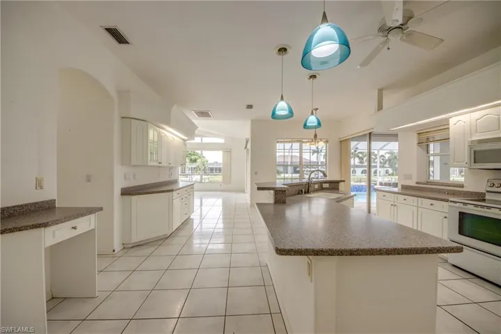 Kitchen with light tile patterned flooring, white appliances, a kitchen island, decorative light fixtures, and sink.  View to the Family Room in the Distance with Water Views