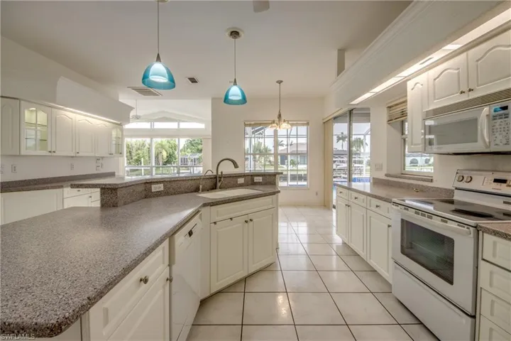 Kitchen featuring white appliances, sink, hanging light fixtures, light tile patterned floors, and a chandelier