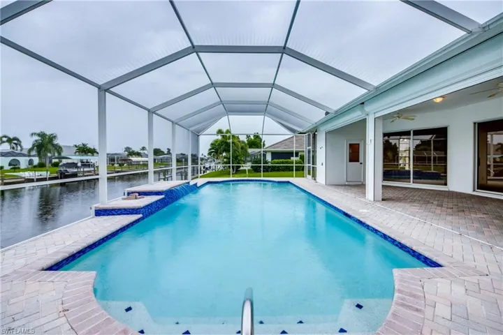 View of swimming pool featuring a patio, ceiling fan, glass enclosure, and pool water feature
