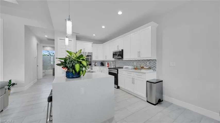 Kitchen featuring light stone counters, white cabinetry, appliances with stainless steel finishes, pendant lighting, and an island with sink