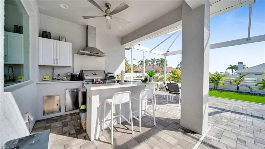 Kitchen featuring a sunroom, light countertops, wall chimney range hood, white cabinetry, and a kitchen breakfast bar