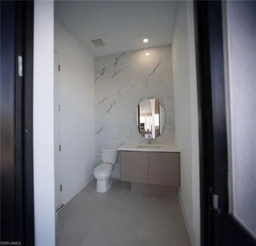 Bathroom featuring vanity, toilet, concrete flooring, and tile walls