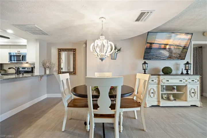 Dining area featuring a decorative chandelier, tile flooring, and a kitchen pass-through with granite-finish countertop