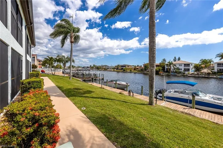 Waterfront property featuring a private boat dock, lush green lawn, mature palm trees, and a paved walkway