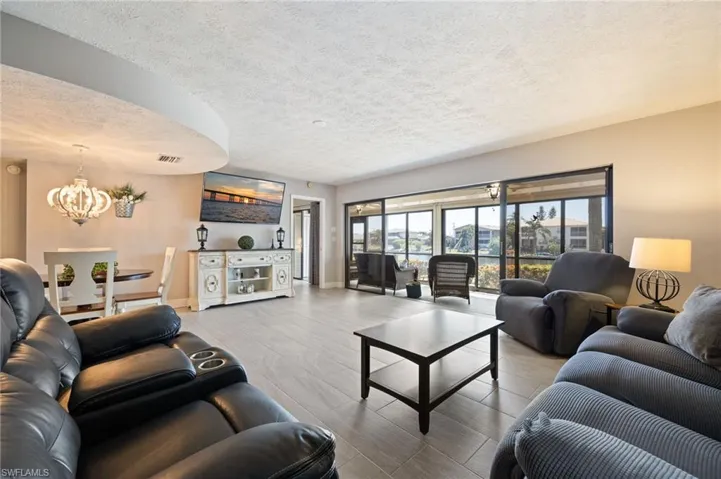Open-concept living area featuring light-toned tile flooring, recessed ceiling details, and a decorative chandelier