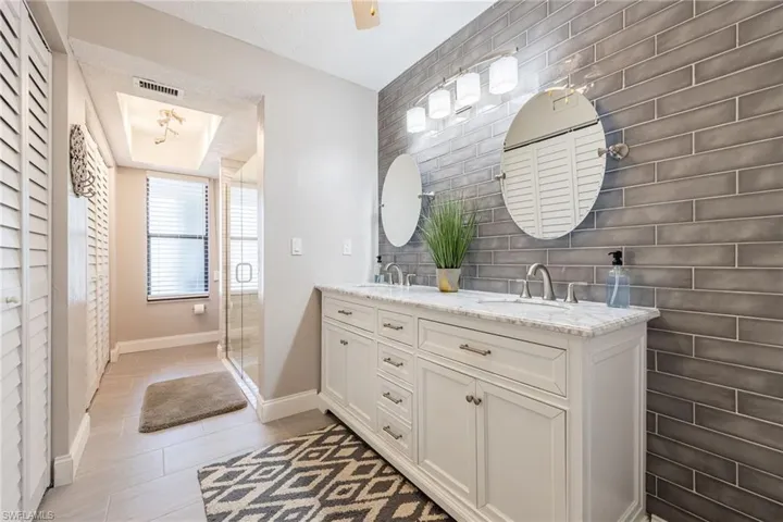 Bathroom featuring a double vanity with marble countertop, individual round mirrors, and a textured subway tile accent wall