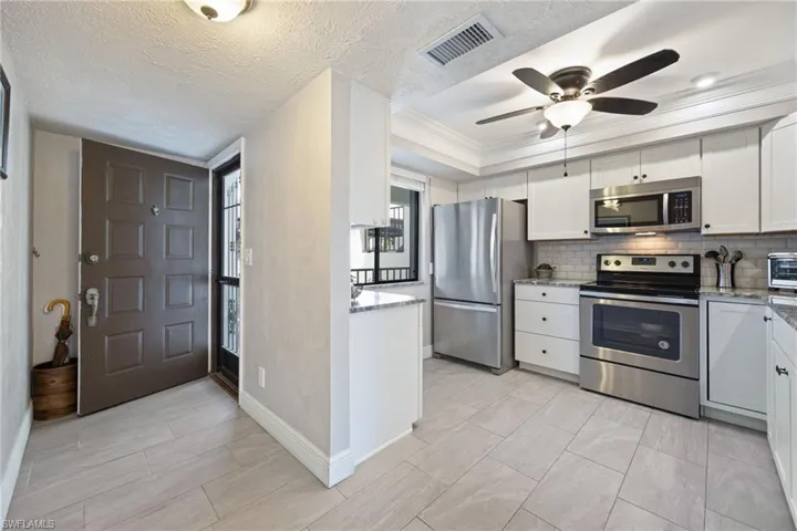 Modern kitchen featuring stainless steel appliances, white cabinetry with dark hardware, and light-toned subway tile backsplash