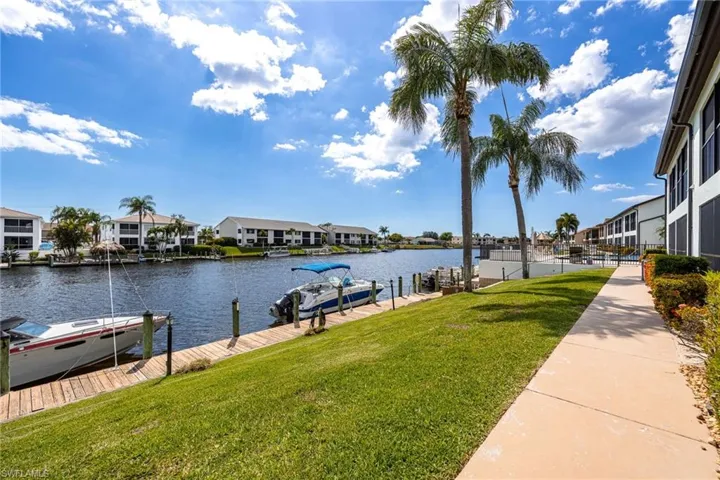 Waterfront canal property featuring a private boat dock, manicured lawn, paved walkway, and established palm trees