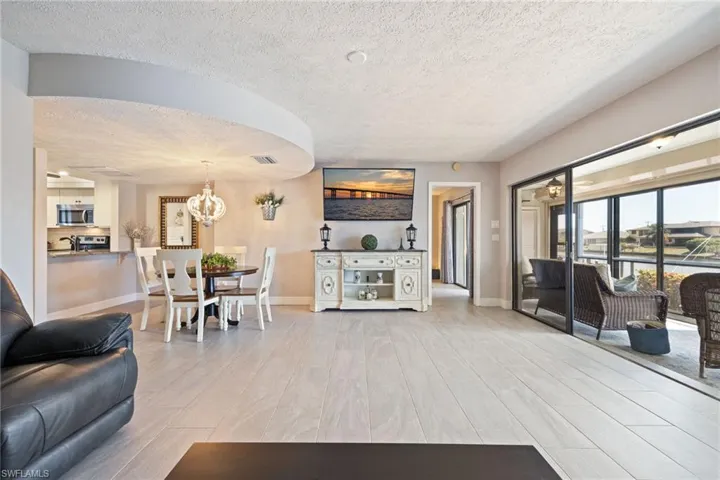 Spacious interior featuring light-toned wood-finish flooring, sliding glass doors to an enclosed patio, and an open layout connecting living and dining areas