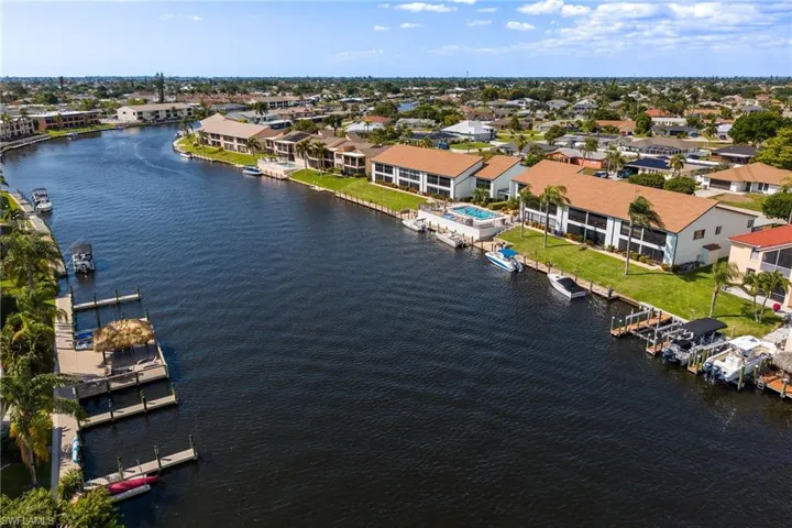 Waterfront property featuring a canal, private boat docks, mature palm trees, a community pool, and a manicured lawn