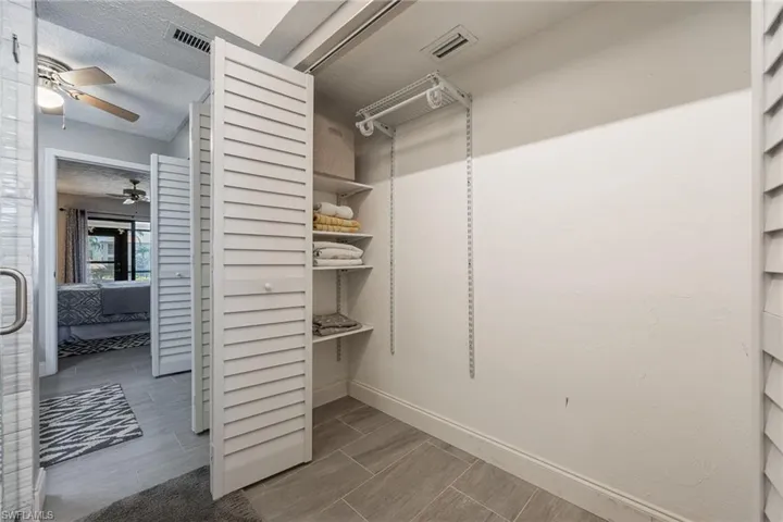 Walk-in closet featuring adjustable shelving, louvered bifold doors, and tile flooring
