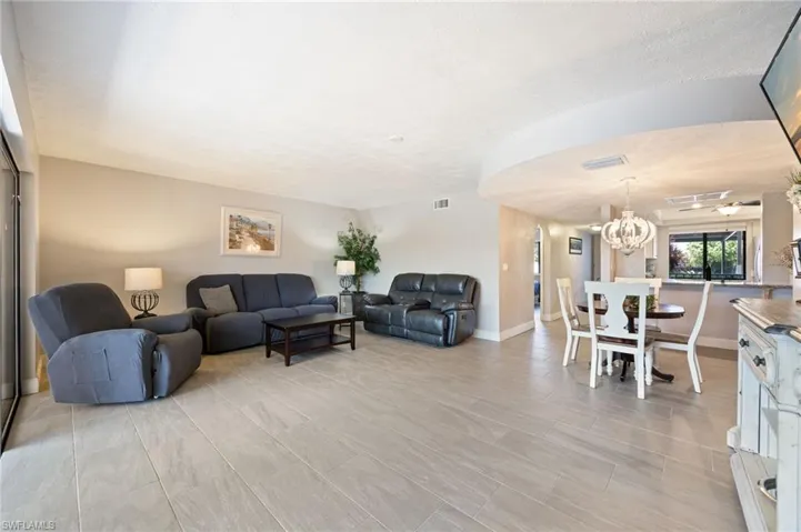 Spacious interior featuring light tone wood-finish tile flooring, neutral wall paint, and a dining area with a decorative chandelier