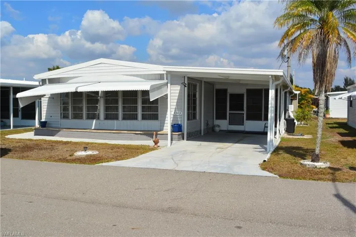 Manufactured / mobile home featuring a sunroom, concrete driveway, an attached carport, and a front yard