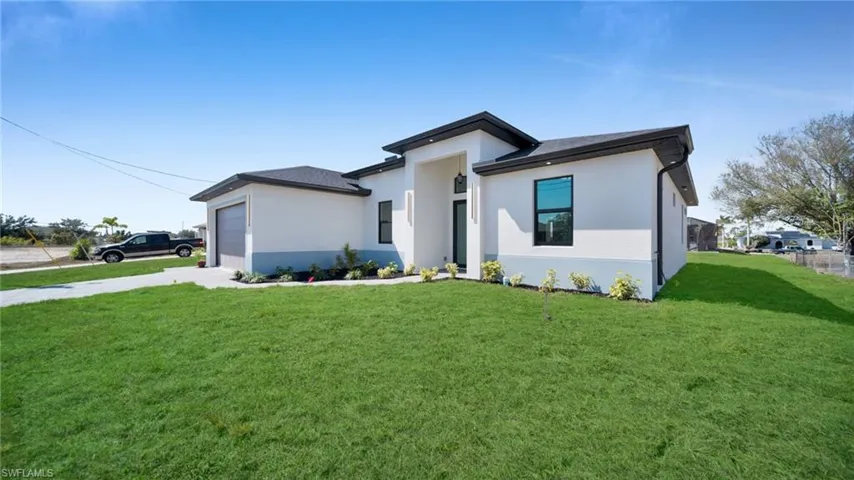 Prairie-style home featuring a front lawn, stucco siding, an attached garage, and driveway