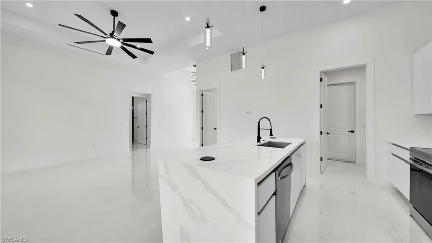 Kitchen featuring pendant lighting, a kitchen island with sink, light stone countertops, white cabinets, and stainless steel appliances