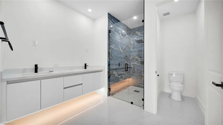 Full bathroom with double vanity, a marble finish shower, and recessed lighting