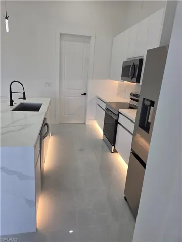 Kitchen with stainless steel appliances, white cabinetry, light stone countertops, and decorative light fixtures