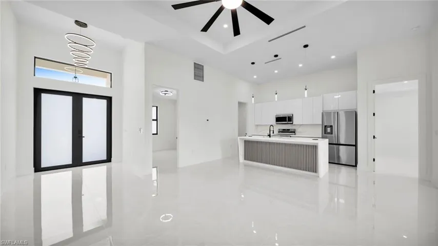 Kitchen featuring stainless steel appliances, white cabinets, a kitchen island with sink, a high ceiling, and open floor plan