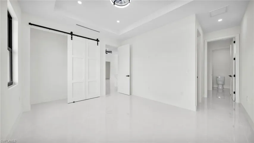 Unfurnished bedroom with a barn door, recessed lighting, a closet, and a raised ceiling