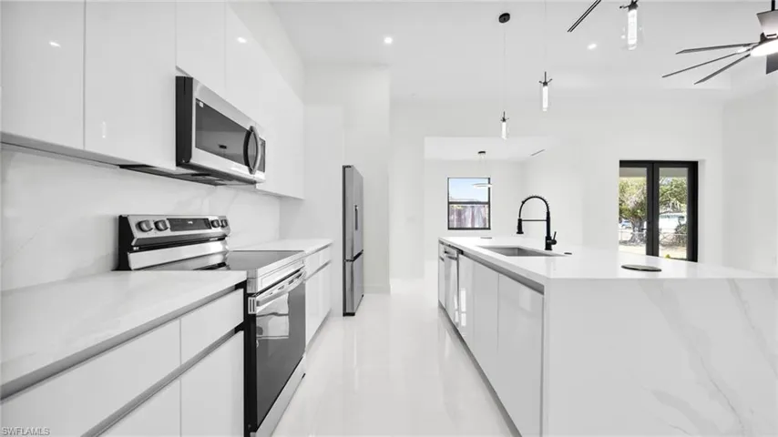 Kitchen featuring stainless steel appliances, a center island with sink, white cabinets, pendant lighting, and modern cabinets
