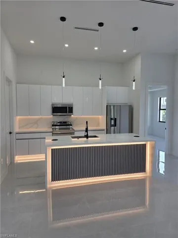 Kitchen featuring white cabinets, stainless steel appliances, pendant lighting, modern cabinets, and a center island with sink