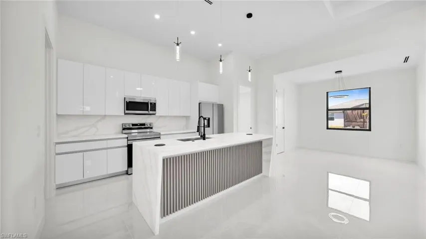 Kitchen with white cabinetry, stainless steel appliances, decorative light fixtures, and a center island with sink