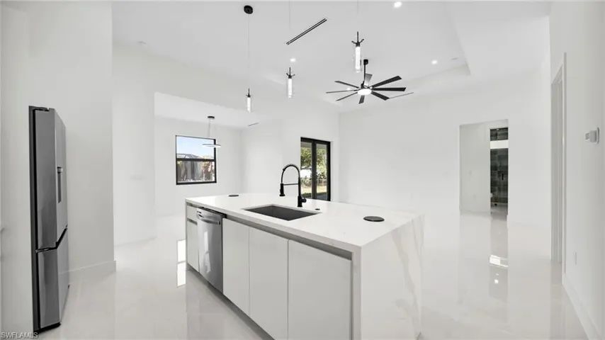 Kitchen with modern cabinets, stainless steel appliances, white cabinets, pendant lighting, and a kitchen island with sink