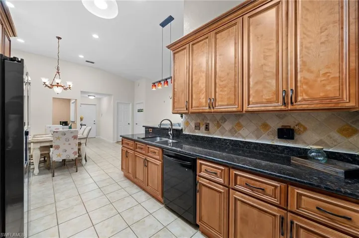 Kitchen featuring a chandelier, sink, hanging light fixtures, black appliances, and dark stone countertops