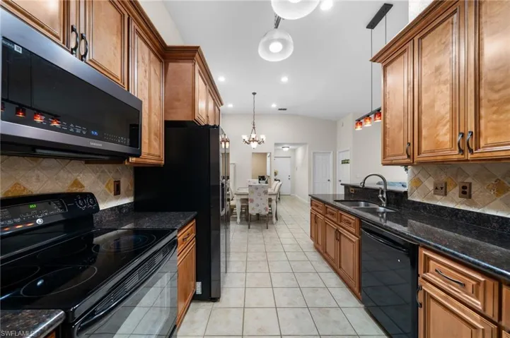 Kitchen featuring decorative light fixtures, backsplash, sink, and black appliances