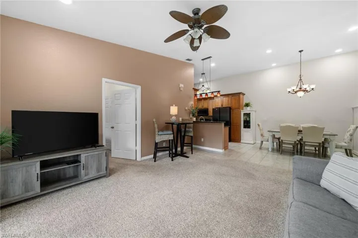 Living room with ceiling fan with notable chandelier and light colored carpet