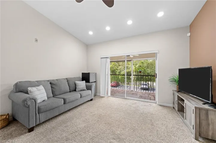 Carpeted living room featuring ceiling fan and vaulted ceiling