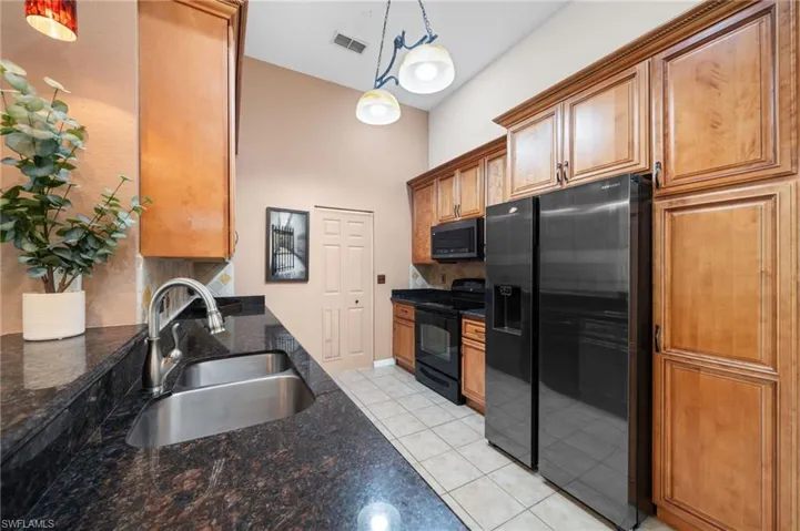 Kitchen with refrigerator with ice dispenser, light tile patterned floors, decorative light fixtures, black electric range oven, and sink