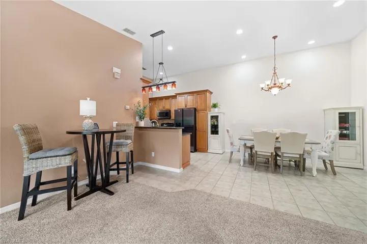 Kitchen with kitchen peninsula, decorative light fixtures, black fridge, light colored carpet, and a notable chandelier