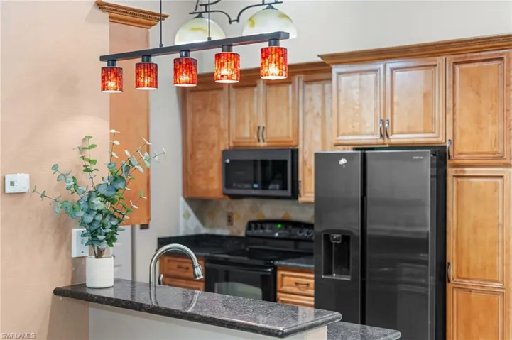 Kitchen with tasteful backsplash, sink, hanging light fixtures, black appliances, and dark stone countertops