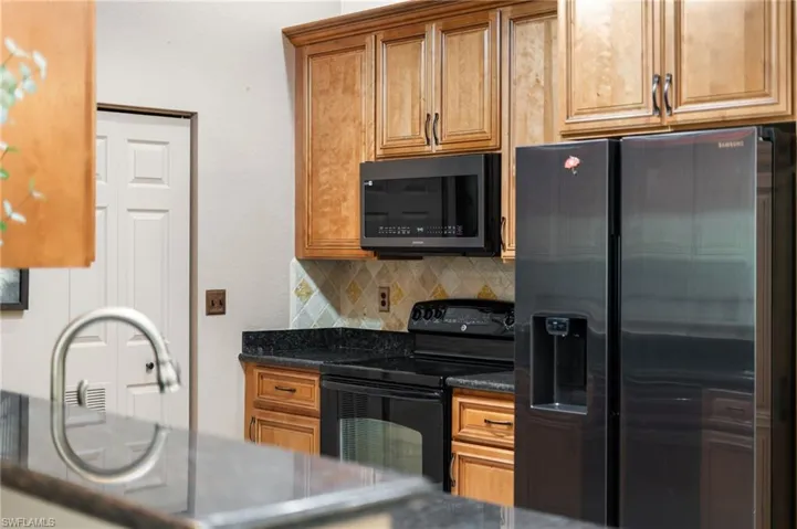 Kitchen featuring decorative backsplash, fridge with ice dispenser, black electric range oven, and dark stone counters