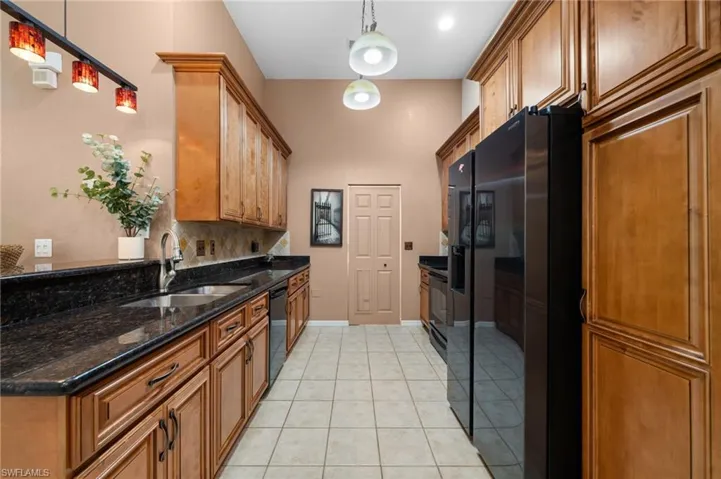 Kitchen with light tile patterned flooring, sink, tasteful backsplash, decorative light fixtures, and black appliances