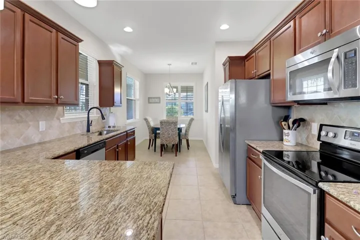 Kitchen appliances with stainless steel finishes, backsplash, light stone counters, sink, and pendant lighting