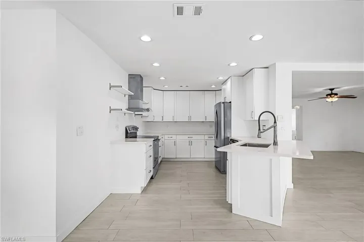 Kitchen with white cabinetry, recessed lighting, stainless steel appliances, a ceiling fan, and a kitchen breakfast bar