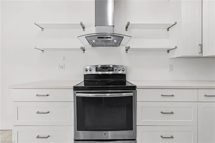 Kitchen featuring electric range, island range hood, white cabinets, open shelves, and light countertops