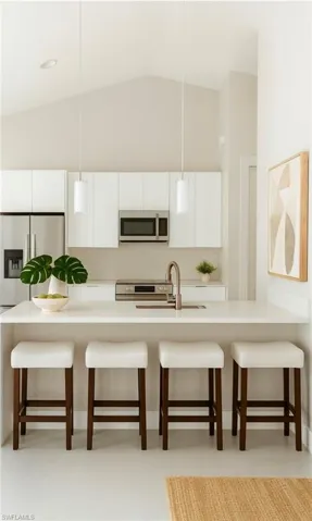 Kitchen featuring a breakfast bar, white cabinets, pendant lighting, stainless steel appliances, and lofted ceiling