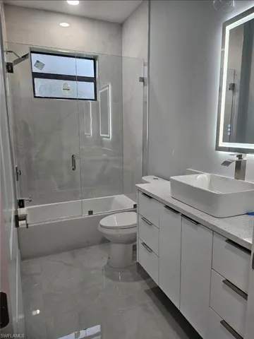 Full bathroom with vanity, bath / shower combo with glass door, and a textured wall