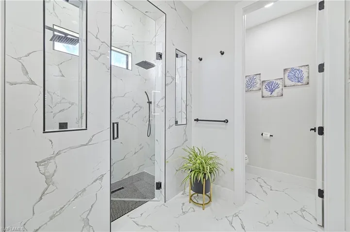 Bathroom with marble finish floor, a marble finish shower, toilet, and baseboards