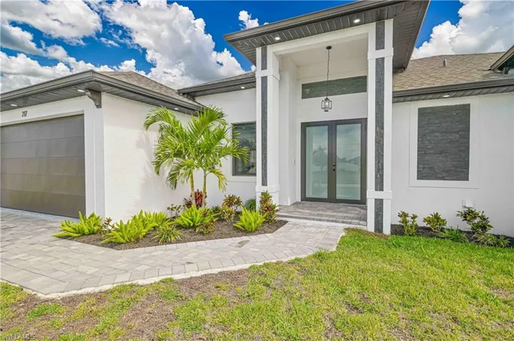 Doorway to property featuring a garage, a shingled roof, a lawn, french doors, and stucco siding