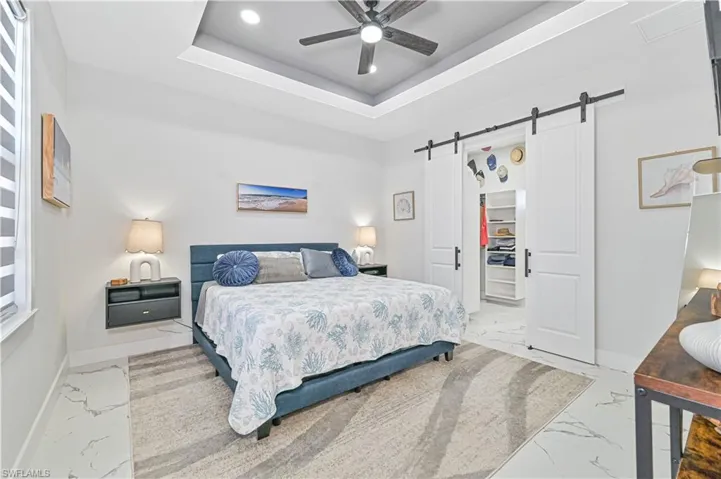 Bedroom with a tray ceiling, marble finish floor, a walk in closet, a barn door, and baseboards