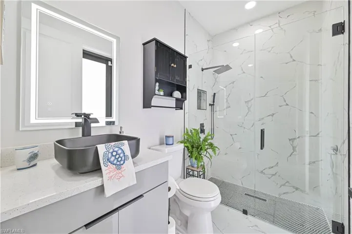 Bathroom featuring marble finish floor, a marble finish shower, recessed lighting, toilet, and vanity