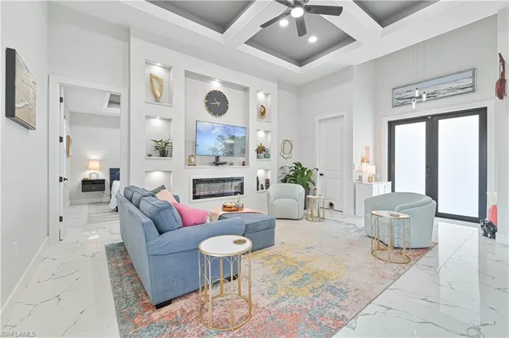 Living room with coffered ceiling, a glass covered fireplace, marble finish floor, a high ceiling, and french doors